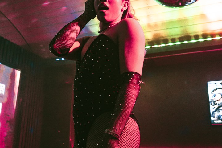 Person in a dark outfit poses under a disco ball with colorful lights.