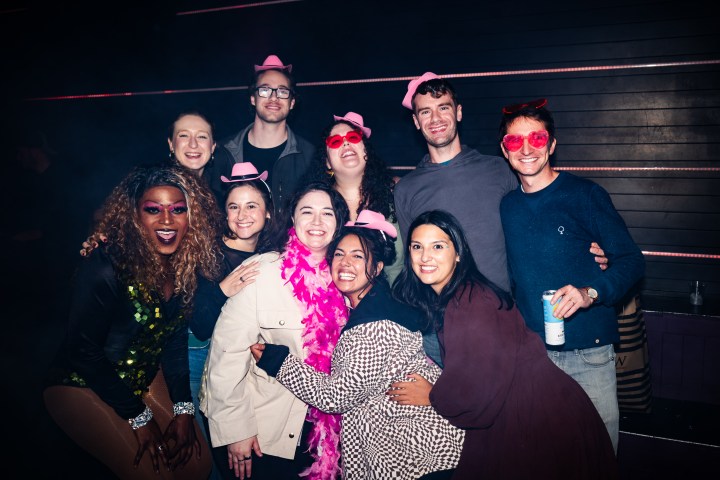 Group of people in party attire with hats and heart-shaped glasses, smiling for a photo.