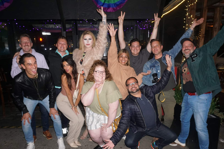 A group of people posing happily with hands raised in a festive, decorated setting at night.