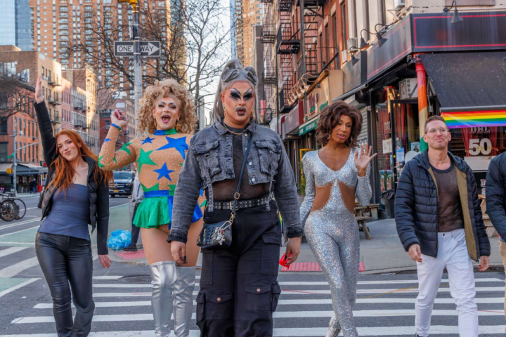 Five people in colorful outfits walking on a city street crosswalk.