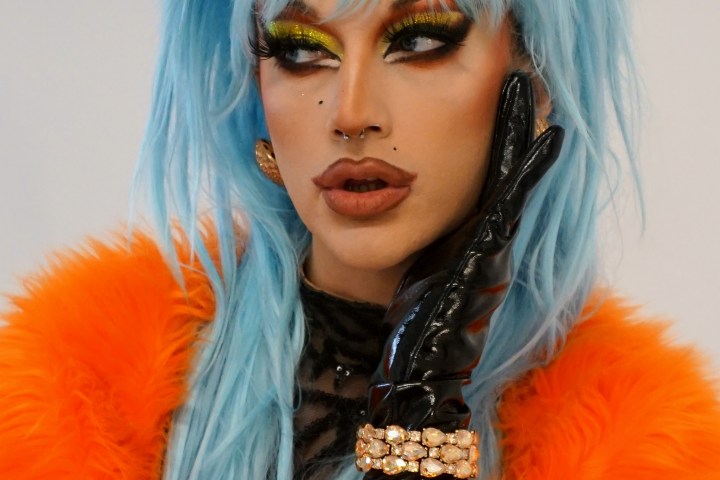 Person with blue hair, heavy makeup, orange fur, black glove.