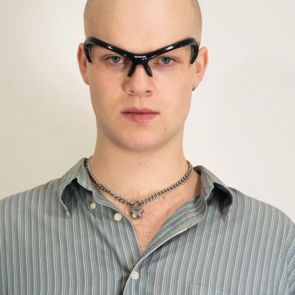 Person with shaved head wearing dark sunglasses, striped shirt, and chain necklace.