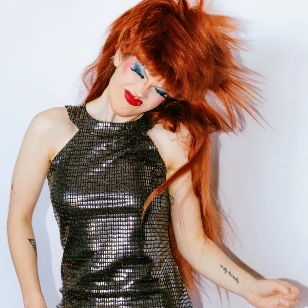 Person with red hair in sequined dress expressing joy on white background.