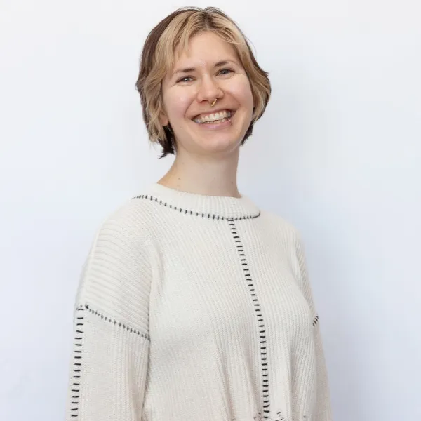 Person smiling, wearing a white sweater with black stitching, against a plain white background.
