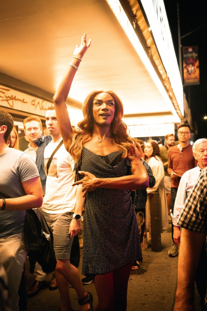 Person in a polka dot dress raises hand in a busy outdoor crowd.